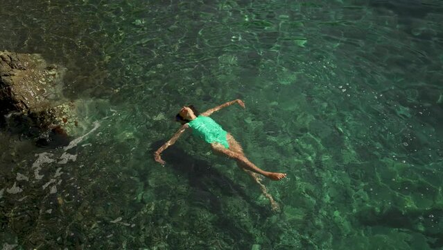 slow motion top view of sexy stunning woman in green swimsuit floating on back and relaxing in clear turquoise water of mediterranean sea. vacation and wellness, Summer Season Fethiye, Turkey