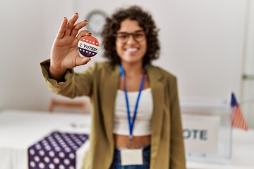 Young hispanic woman smiling confident holding i voted badge at electoral college - obrazy, fototapety, plakaty