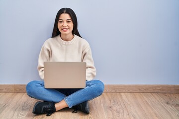 Young woman using laptop sitting on the floor at home with a happy and cool smile on face. lucky person.