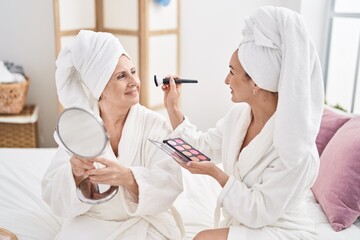 Mother and daughter wearing bathrobe applying makeup at bedroom