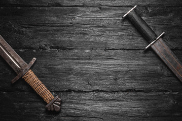 Two ancient swords on the black wooden table flat lay background with copy space.