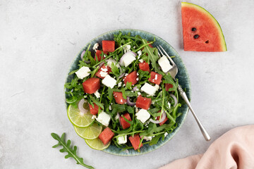 Green salad of watermelon, feta cheese and arugula on a gray background. Vegan, European food.