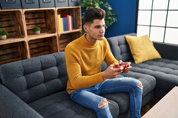 Obraz premium Young hispanic man playing video game sitting on sofa at home