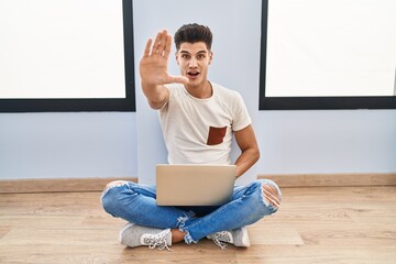 Young hispanic man using laptop at home doing stop gesture with hands palms, angry and frustration expression