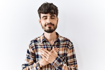 Hispanic man with beard standing over isolated background smiling with hands on chest with closed eyes and grateful gesture on face. health concept.