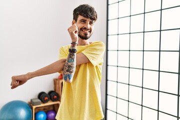 Young hispanic man smiling confident stretching at sport center.