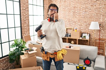 Fototapeta na wymiar Handsome middle age man holding screwdriver at new home looking stressed and nervous with hands on mouth biting nails. anxiety problem.