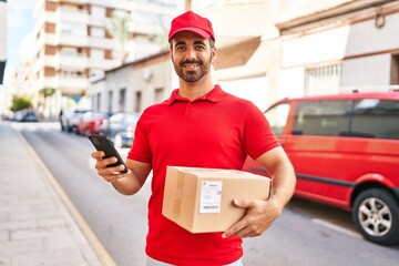 Young hispanic man courier using smartphone holding package at street
