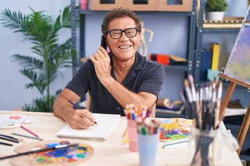 Fototapeta premium Middle age man artist talking on smartphone drawing on notebook at art studio