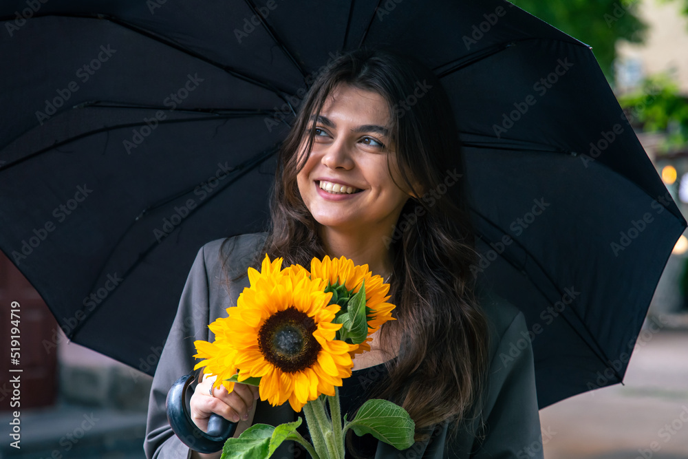 Wall mural A young woman with a bouquet of sunflowers under an umbrella in rainy weather.