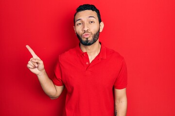 Fototapeta premium Hispanic man with beard pointing with fingers to the side looking at the camera blowing a kiss being lovely and sexy. love expression.