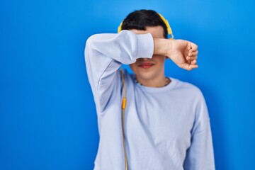 Non binary person listening to music using headphones covering eyes with arm smiling cheerful and funny. blind concept.