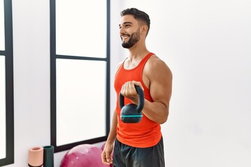 Young arab man smiling confident training with kettlebell at sport center