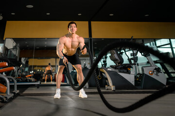Fototapeta na wymiar Young Asian man works out with battle ropes in a healthy fitness gym. Asian man with battle rope battle ropes exercise in the fitness gym.