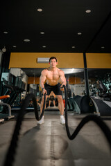 Young Asian man works out with battle ropes in a healthy fitness gym. Asian man with battle rope battle ropes exercise in the fitness gym.