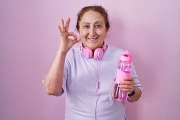 Senior woman wearing sportswear and headphones smiling positive doing ok sign with hand and fingers. successful expression.