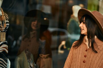 Naklejka premium Brunette woman wearing winter hat looking at shop window outdoors at the city