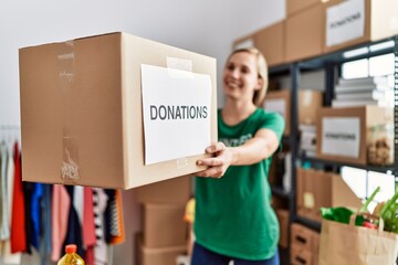 Young caucasian woman wearing volunteer uniform holding donations package working at charity center