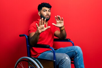 Arab man with beard sitting on wheelchair moving away hands palms showing refusal and denial with...