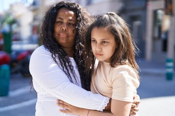 Mother and daughter hugging each other with serious expression at street