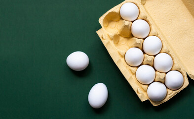 Many eggs stand in a yellow paper box on a dark green background - 519196543