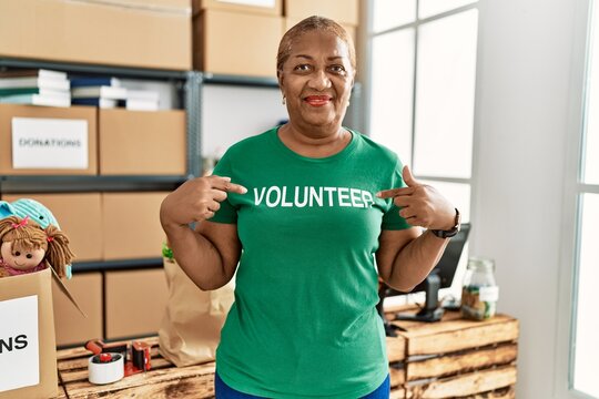 Senior african american woman pointing with fingers to volunteer uniform at charity center