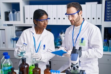 Man and woman scientists using touchpad measuring liquid at laboratory