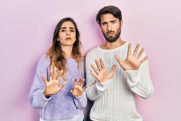 Young hispanic couple wearing casual clothes moving away hands palms showing refusal and denial...