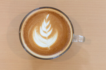 Top view of white leaf pattern coffee latte art in cup on isolated wood table background, flat lay, copy space for text.
