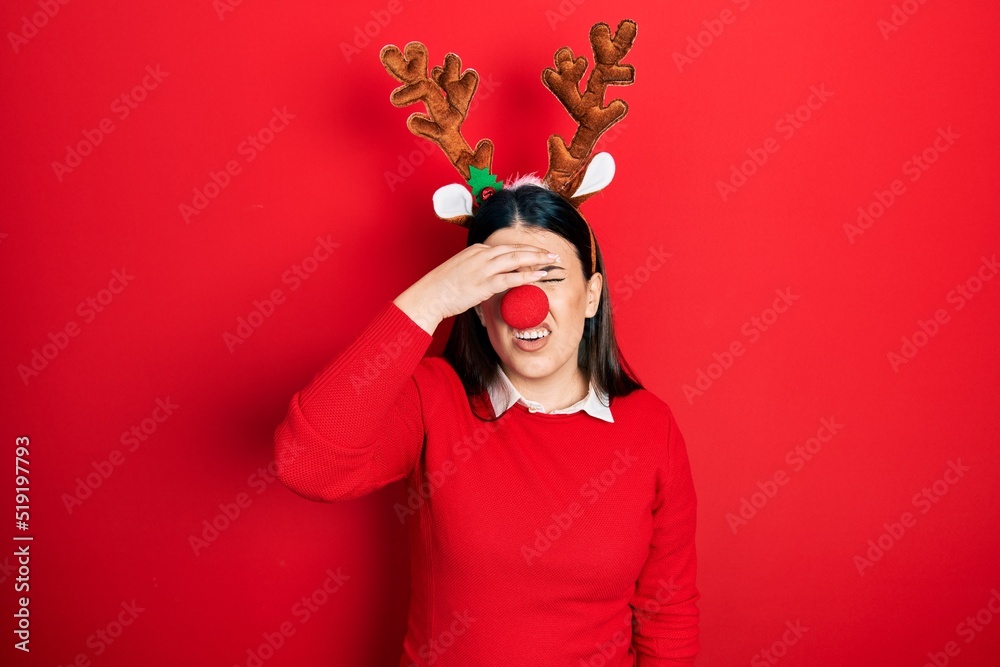 Sticker Young hispanic woman wearing deer christmas hat and red nose tired rubbing nose and eyes feeling fatigue and headache. stress and frustration concept.