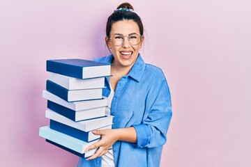 Young hispanic woman wearing glasses and holding books smiling with a happy and cool smile on face. showing teeth.