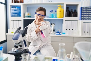Hispanic girl with down syndrome working at scientist laboratory in hurry pointing to watch time, impatience, looking at the camera with relaxed expression