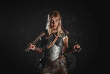 Warrior woman in the armor stands with the two swords in the hands concept.