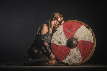 Fototapeta premium Woman warrior in the armor and with the sword and shield in hands stands on her knees. Lose the battle concept.