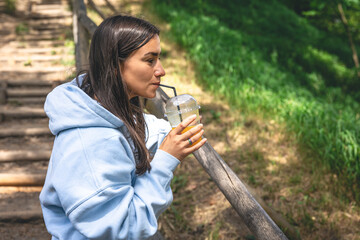 A young woman drinks juice from a straw in the park.