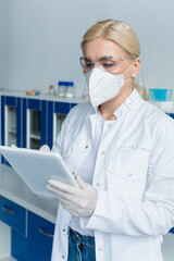 Scientist in protective mask and goggles using digital tablet in lab.