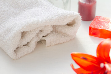 White towel, a soap bar, a candle,  a red flower on white background. Spa concept