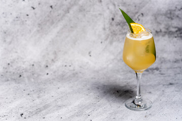 Beautiful yellow cocktail with orange slice garnished with green leaf on concrete background. Long stem glass. Free space for your text