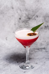 Beautiful red cocktail garnished with dried orange and green leaf on a concrete background. Long stem glass