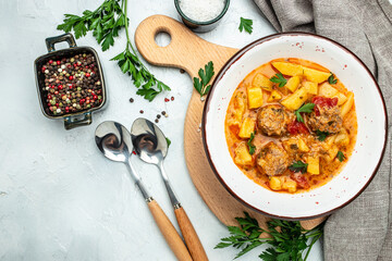 stew called lecho meatball, potato, onion, zucchini with tomato sauce, garlic and herbs in a white bowl, banner, menu, recipe place for text, top view