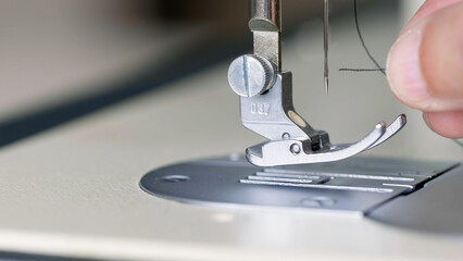 Preparation for sewing. Seamstress inserts thread in needle of sewing machine, side view. Tailor is working in workshop. Sewing workshop. Concept of Factory, Home, At Work, Professionals