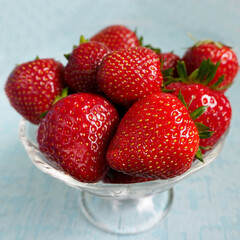 juicy red strawberry in a glass plate stands on a blue background.  summer berries