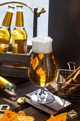 Close-up of an elegant glass with fresh light beer on a wooden table. Delicious natural drink with snacks in the pub.