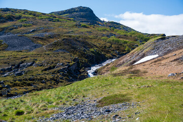 Fototapeta na wymiar Hill with stream, grass, snow and stones