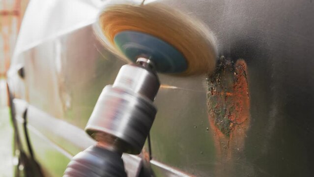 A round metal brush in the hands of the master cleans rust and paint from the car. Medium plan