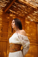 Stylish woman in knitted dress looking away in wooden bungalow at resort in summer