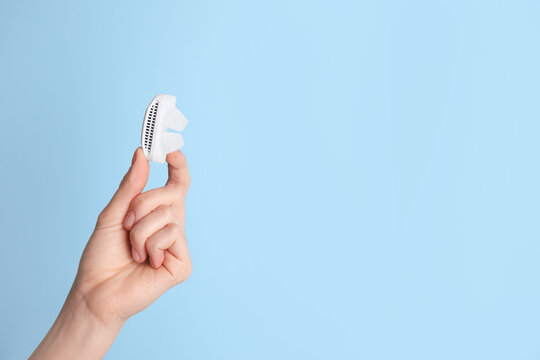 Woman holding anti-snoring device on light blue background, closeup. Space for text