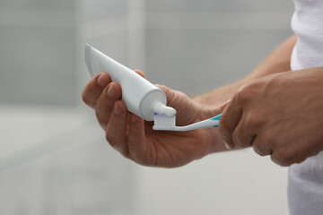 Man applying toothpaste on brush in bathroom, closeup