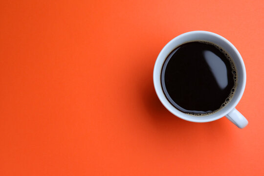 White mug of freshly brewed hot coffee on orange background, top view. Space for text