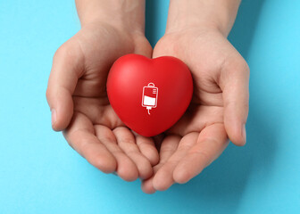 Man holding red heart in hands on light blue background, top view. Blood donation concept